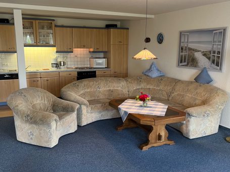 Gemütliche Sitzecke mit Couch, Sessel und Tisch, umgeben von Holzschränken in einer Wohnküche.
